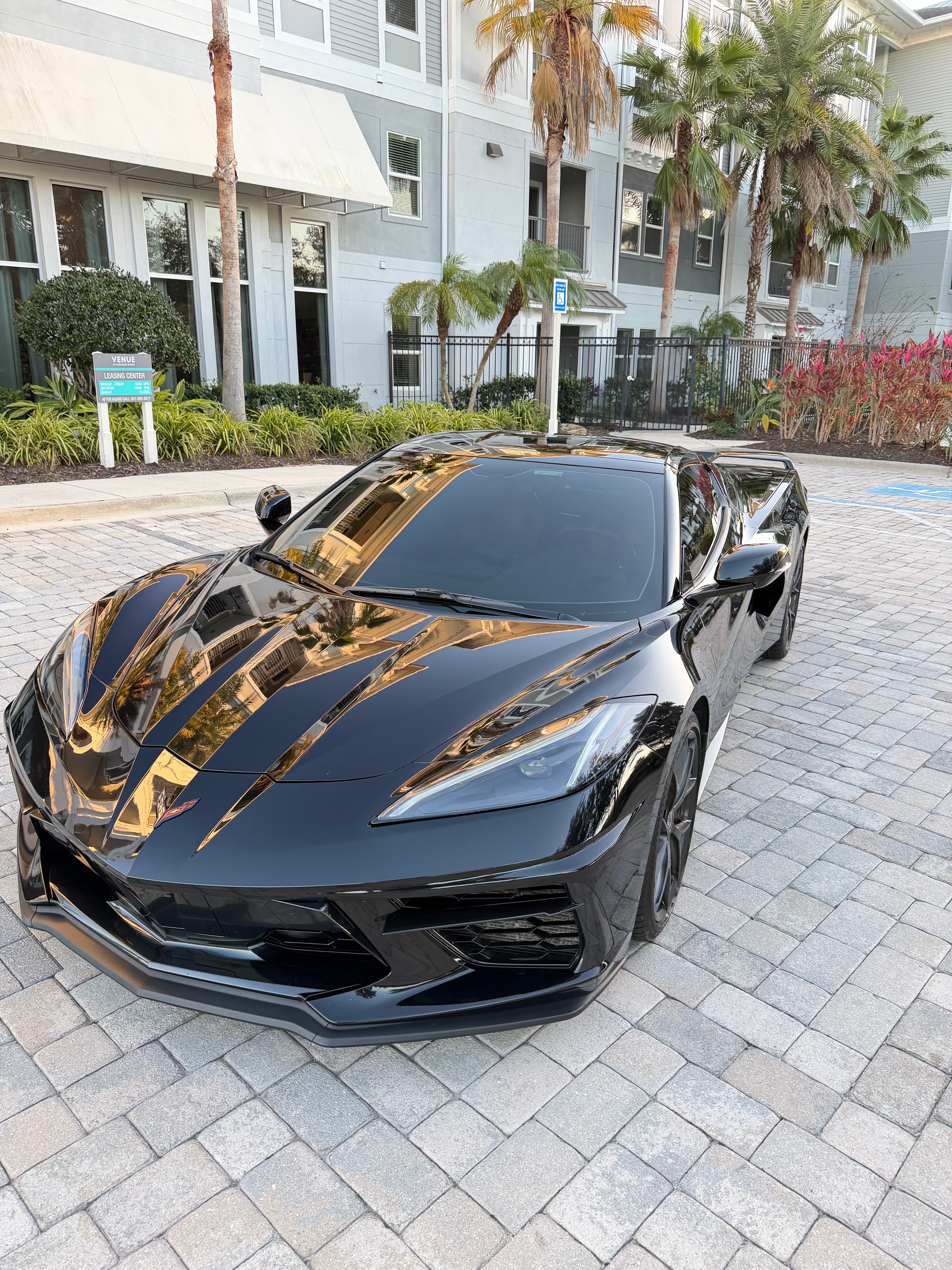 Sleek black Chevrolet Corvette parked on a stone-paved driveway in front of a modern building.